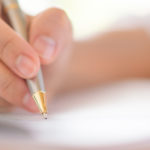 image d'une main en train d'écrire sur un cahier avec un stylo